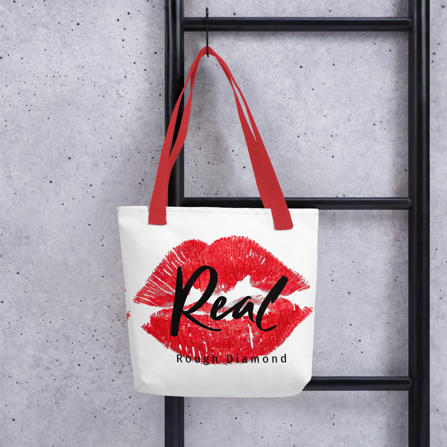 white tote bag with red lip graphic stating Real, Rough Diamond Apparel hanging on a ladder