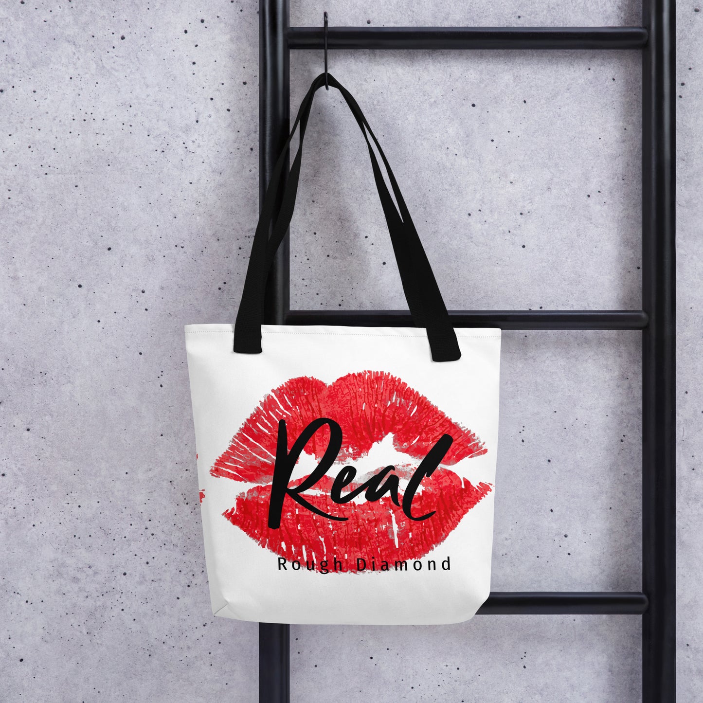 white tote bag with red lip graphic stating Real, Rough Diamond Apparel hanging on a ladder