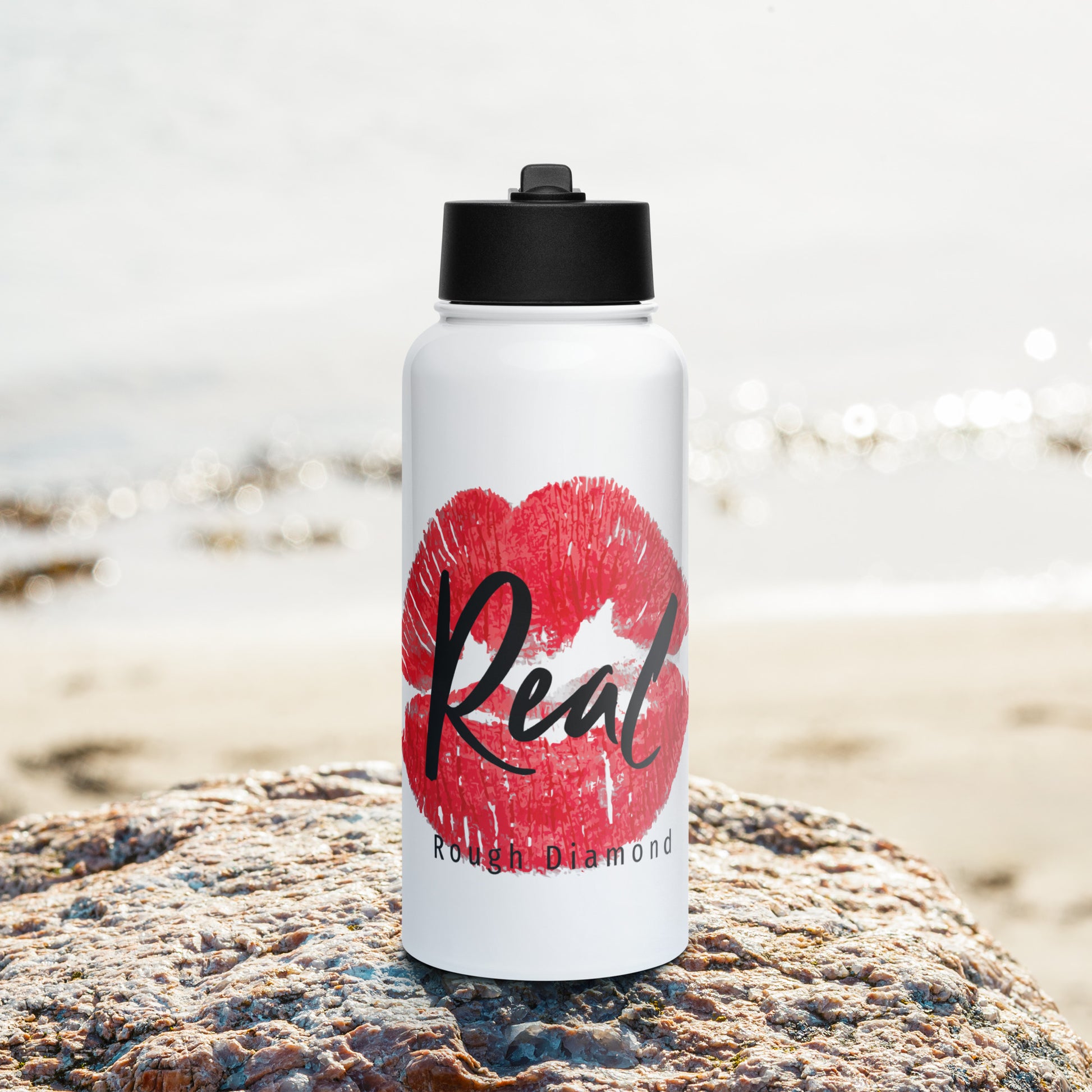 Rough Diamond white water bottle with Real red lips graphic sitting on a rock in a beach setting