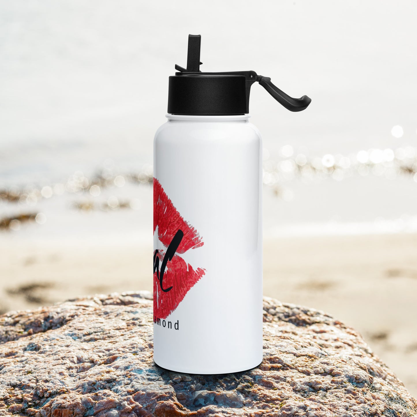 Rough Diamond white water bottle with Real red lips graphic sitting on a rock in a beach setting left side view