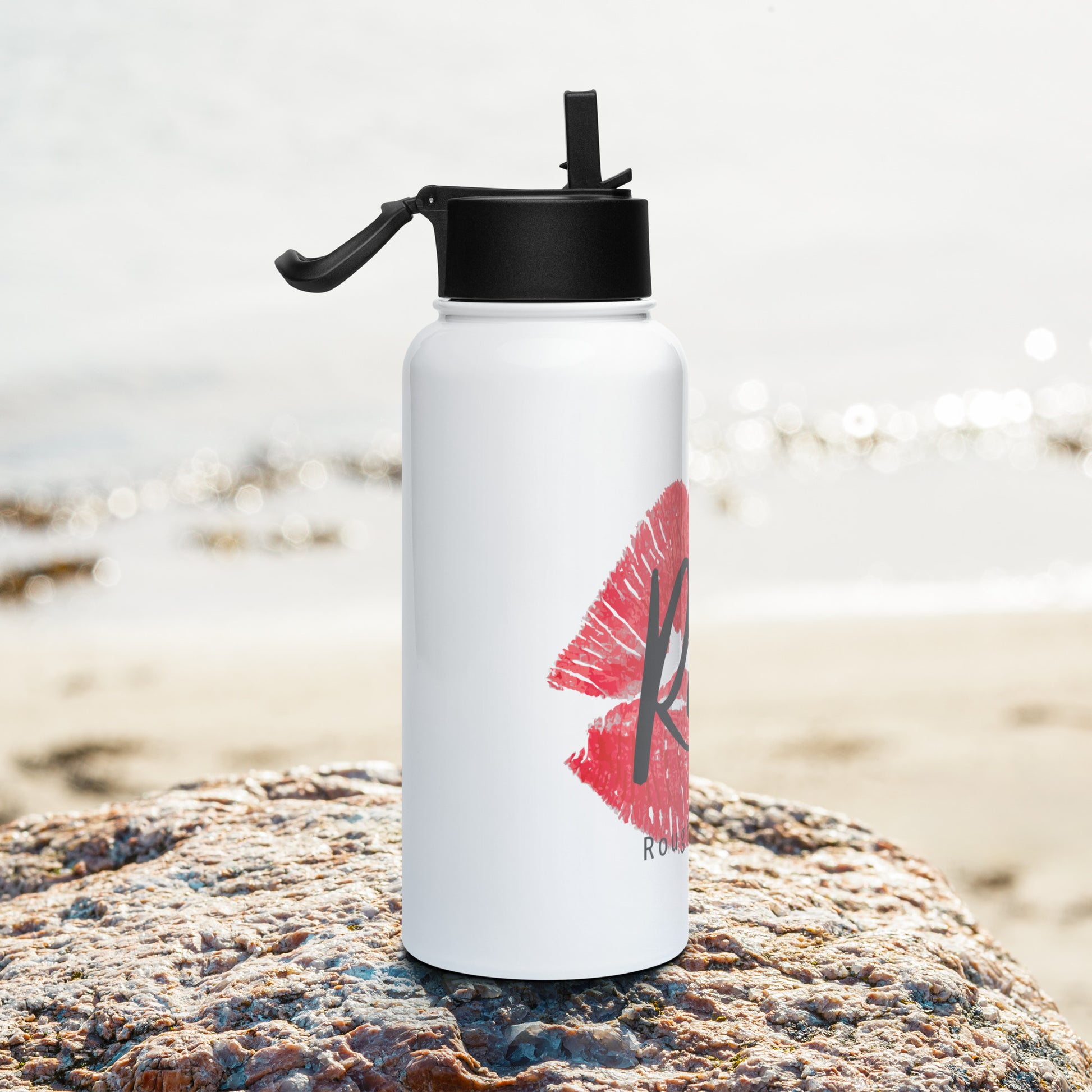 Rough Diamond white water bottle with Real red lips graphic sitting on a rock in a beach setting right side view